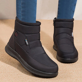Black winter boots worn with blue jeans on a beige surface