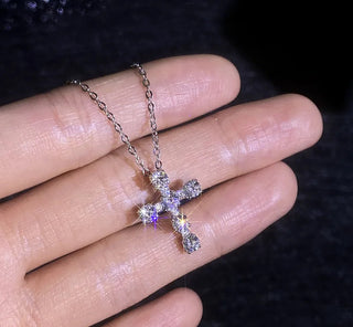Silver cross necklace on a hand with a dark background