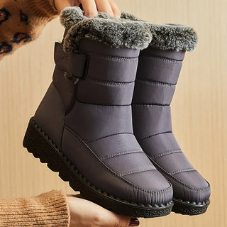 Pair of gray winter boots with fuzzy lining held by a person against a beige background