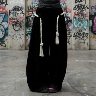 Woman in a black strapless top and long skirt holding a drink outdoors.